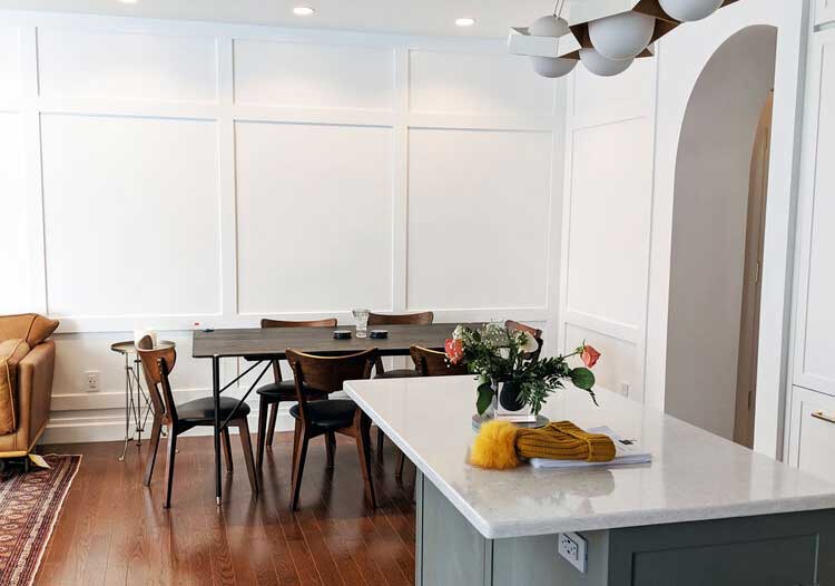 Cuisine ouverte et salle à manger avec un îlot central, chaises en bois, et éclairage moderne, créant un espace de vie chaleureux et lumineux.