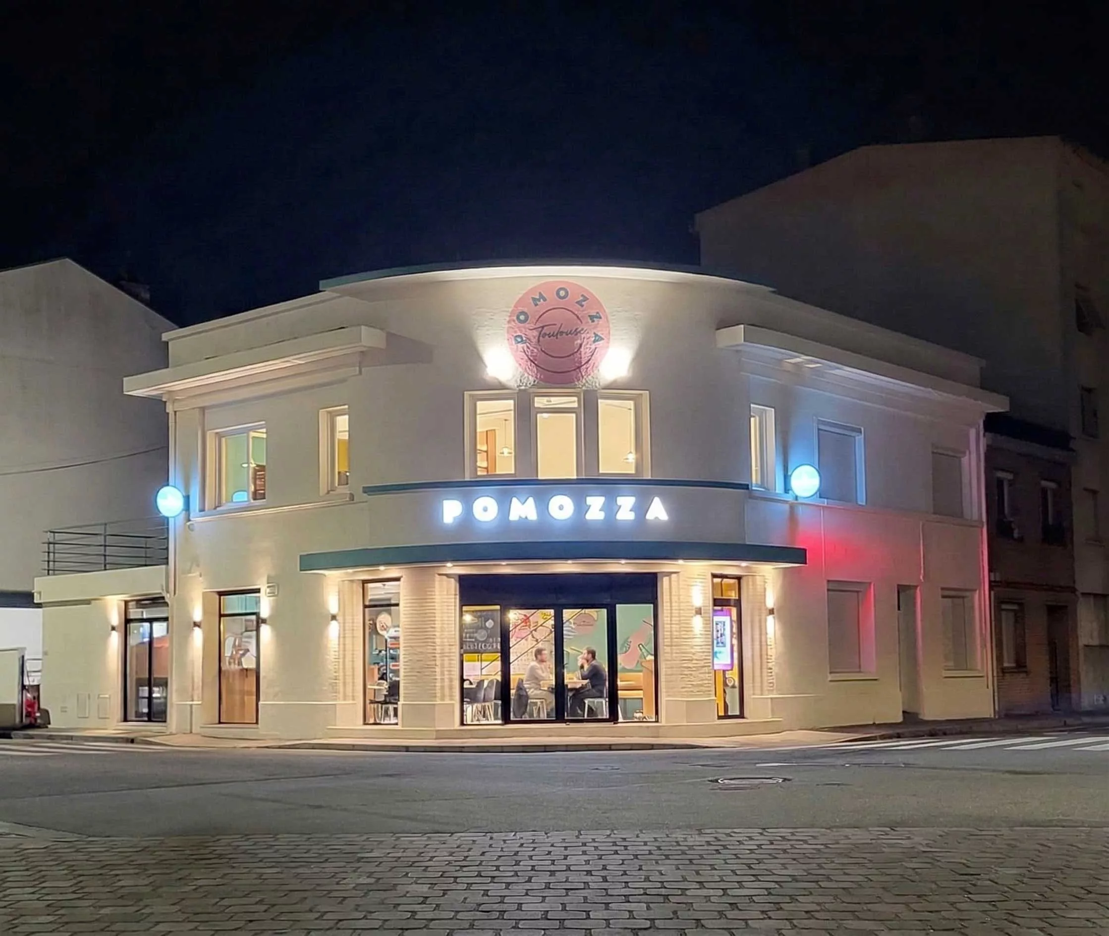 Façade en angle du restaurant Pomozza à Toulouse : enseigne lumineuse et fresque murale, de nuit